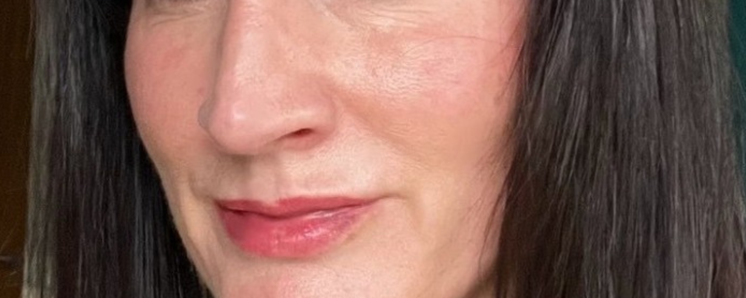 Close-up of a woman’s face showcasing glowing, radiant skin. The image highlights the smooth texture of her skin with a natural glow and soft makeup, including subtle pink lips. The woman has long, dark hair and is wearing a pair of hoop earrings. The glowing skin effect emphasises the skincare benefits of Face Junkie products, promoting healthy, luminous skin.
