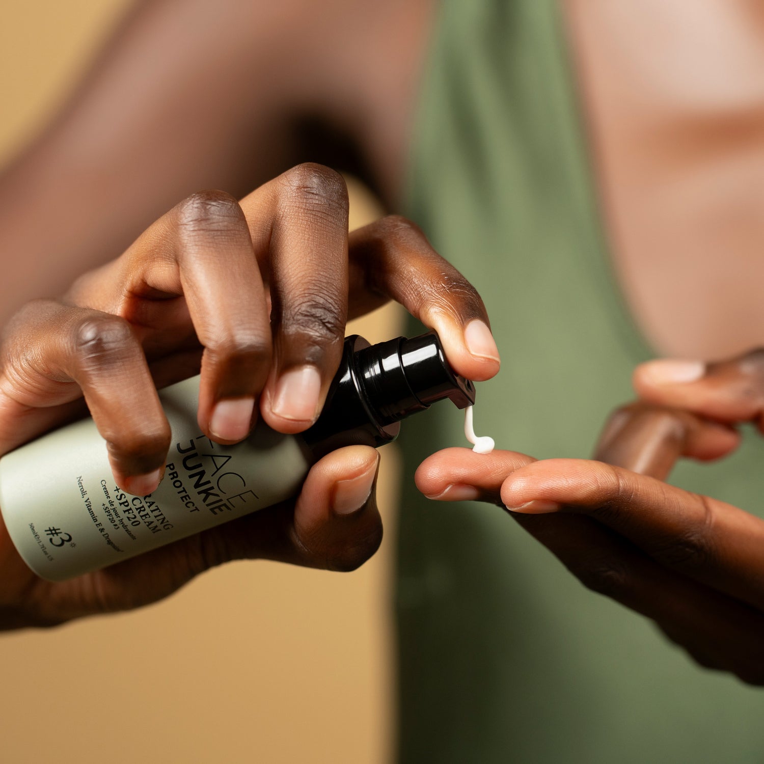 The image shows a person applying a skincare product by dispensing it from a pump bottle onto their fingers. The product is labeled "FACE JUNKIE Protect Hydrating Cream SPF," suggesting it is a moisturizing sunscreen. The person&