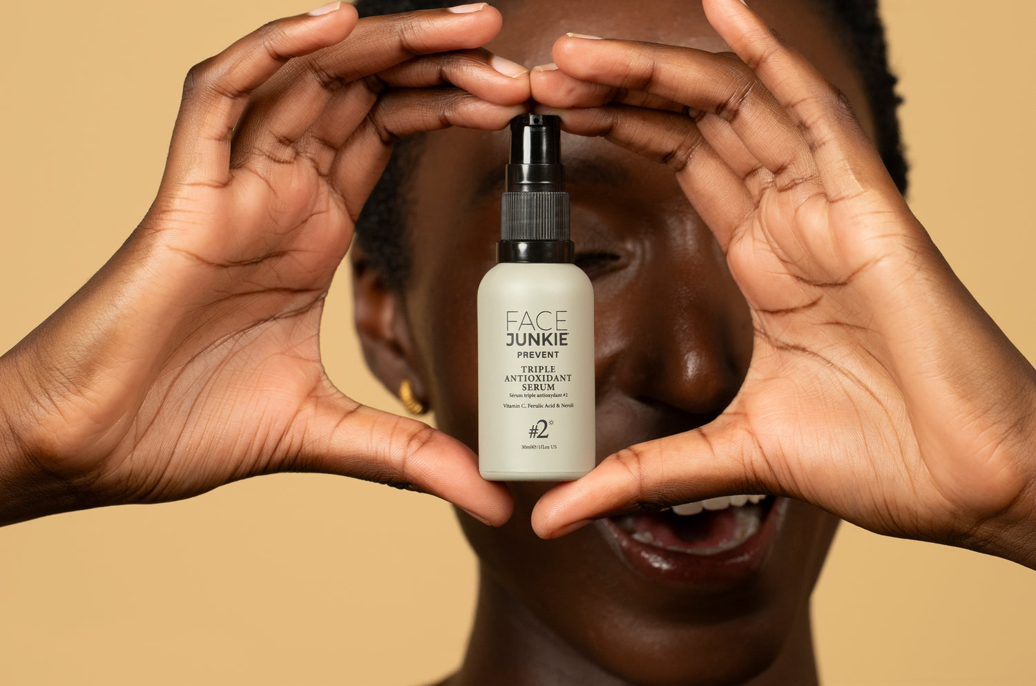 Face Junkie Triple Antioxidant Serum held by a model with glowing skin against a warm beige background. Skincare product featuring Vitamin C, Ferulic Acid, and Neroli for skin protection and radiance. Clean beauty, antioxidant serum, skincare photography.