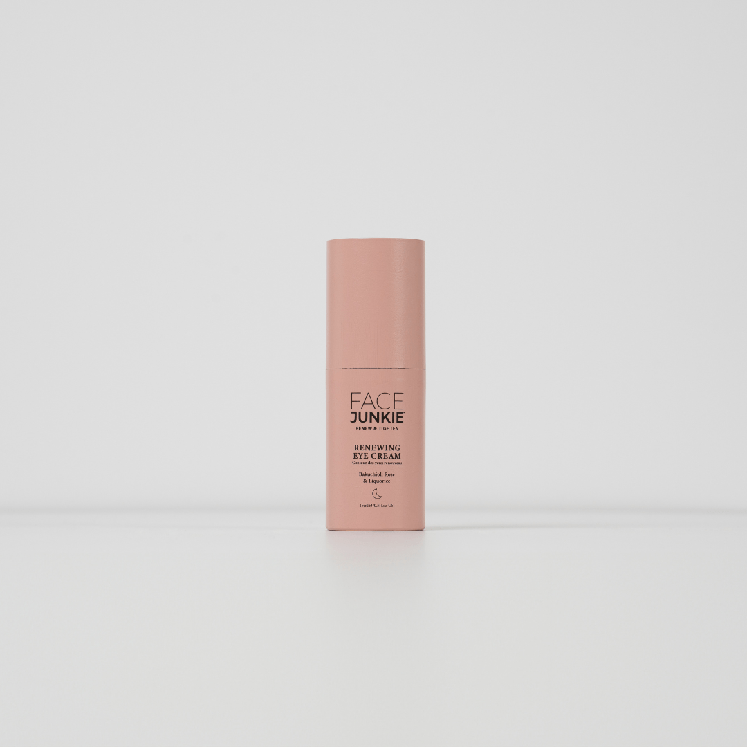 The image displays a single bottle of a skincare product standing upright against a plain white background. The product is labeled "FACE JUNKIE Renewing Eye Cream," and the bottle is a soft pink color with a minimalist design. The text on the bottle mentions that the cream contains beneficial ingredients like Bakuchiol, Rose, and Caffeine, intended for eye care. The packaging is sleek and simple, creating a clean and modern aesthetic.