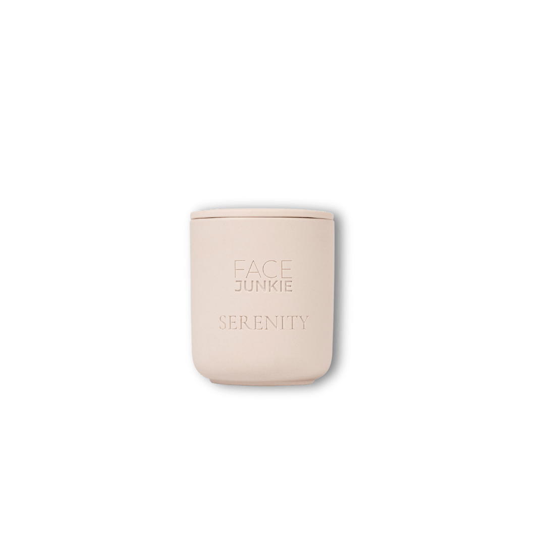 A light pink candle from Face Junkie, with the word "SERENITY" engraved below the brand logo. The minimalist design of the candle conveys a soft, calming ambiance, perfect for relaxation and self-care. The candle is displayed against a transparent background, allowing focus on its simple yet elegant appearance.