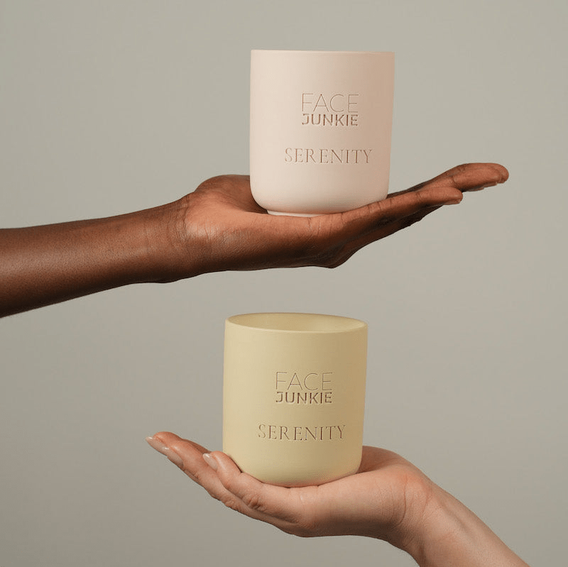 Face Junkie Serenity candles in minimalist, matte pastel containers, elegantly held by two hands of different skin tones against a neutral background. These luxury wellness candles promote relaxation, mindfulness, and self-care, aligning with Face Junkie’s holistic approach to beauty and well-being. The aesthetic design and calming ambiance make them a perfect addition to any self-care ritual.