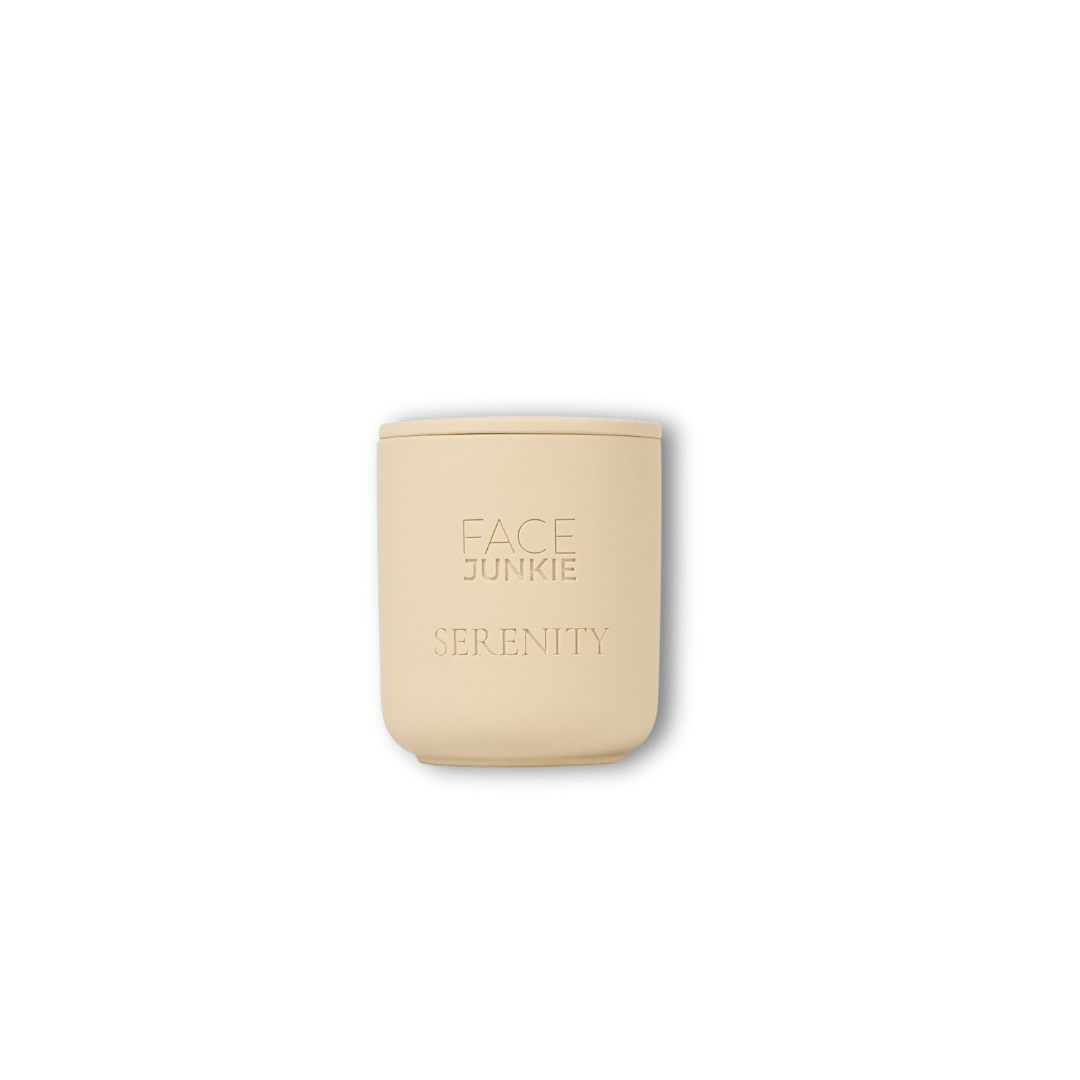 A cream-colored candle from Face Junkie with the word "SERENITY" engraved below the brand logo. The minimalist, sleek design of the candle reflects a calm and soothing aesthetic, aligning with the theme of relaxation and self-care. The background is transparent, drawing full attention to the candle&